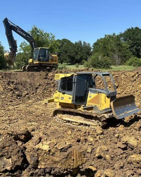 Yellow excavator and bulldozer on a dirt construction site under a clear blue sky