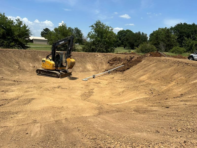 Yellow excavator on a dirt construction site with graded slopes and trees in the background