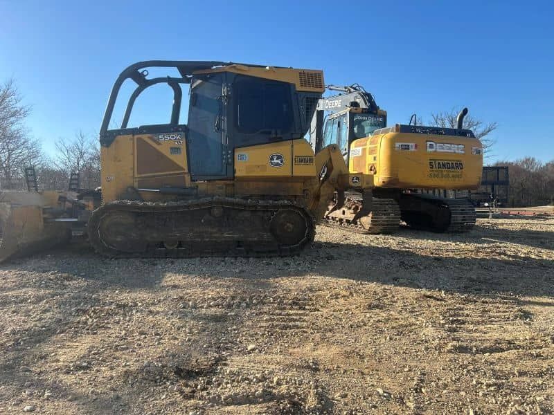 A yellow bulldozer and excavator on a cleared dirt lot under a clear blue sky