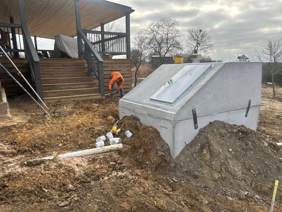 Concrete storm shelter being installed in front of porch steps and worker in orange