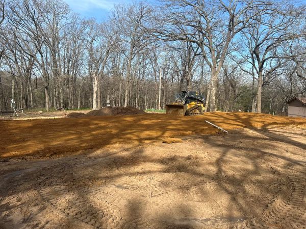 Bulldozer leveling a dirt lot in a wooded area under a clear blue sky