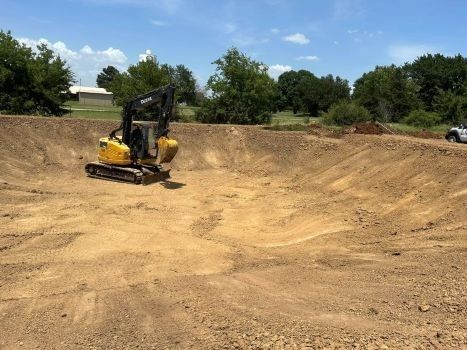 Construction crew digging a trench beside a yellow excavator on a dirt lot