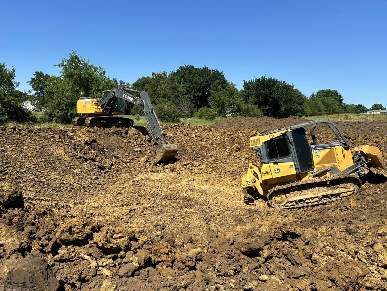 An excavator and bulldozer digging a pond under a clear blue sky
