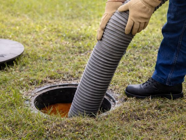 Worker inserting corrugated hose into an open manhole in grassy ground