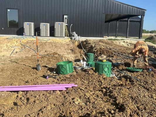 Aerobic Septic System Installation and Maintenance Construction site beside a dark metal building, with excavated dirt, green aerobic septic equipment, and purple pipes.