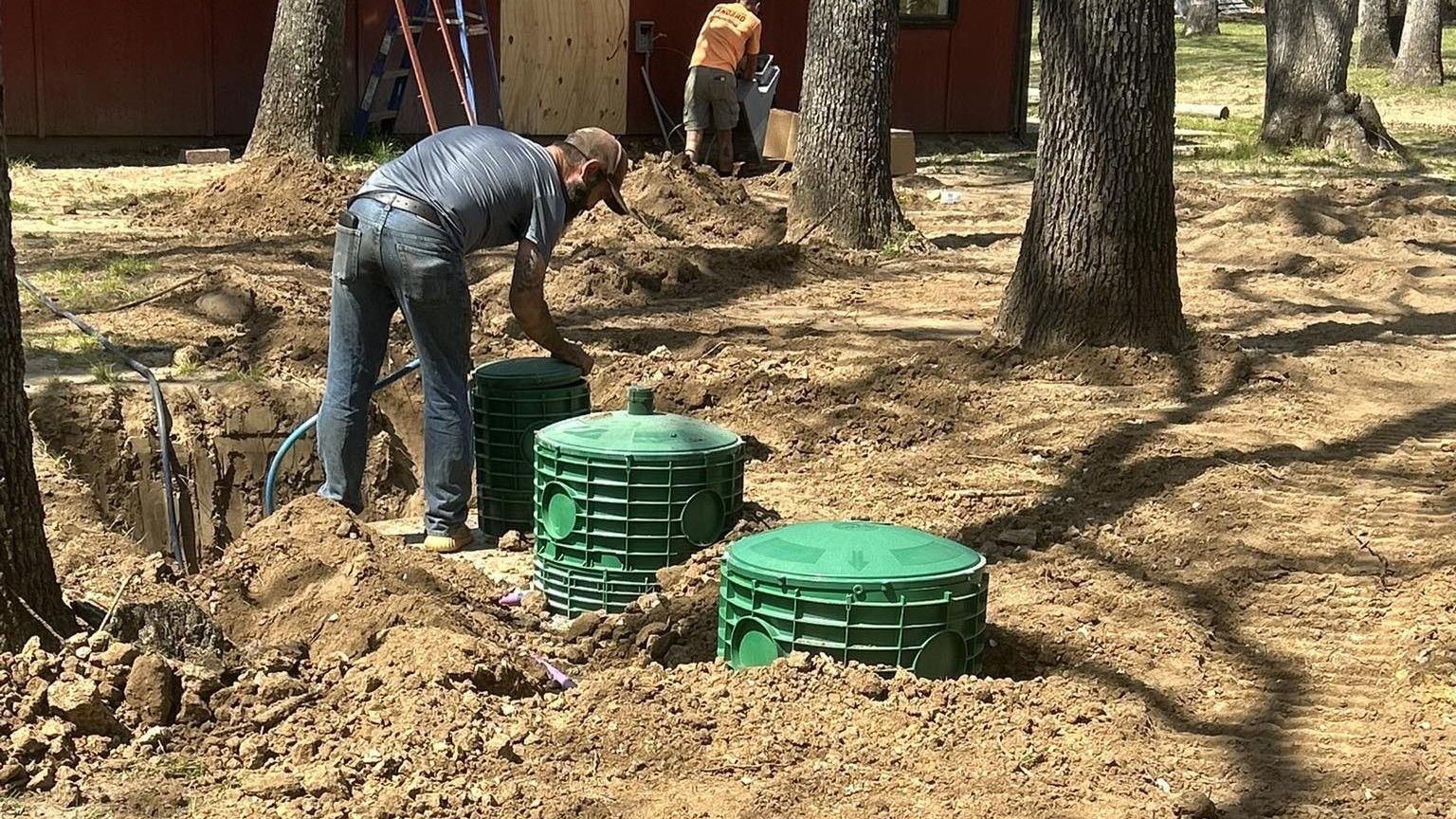 Worker bending over green utility covers in a wooded construction area