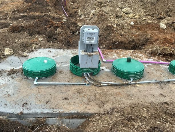 Utility boxes and green sewer caps in a dirt trench at a construction site