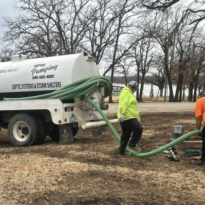 Workers pumping out a septic tank with a white tanker truck in a wooded outdoor area