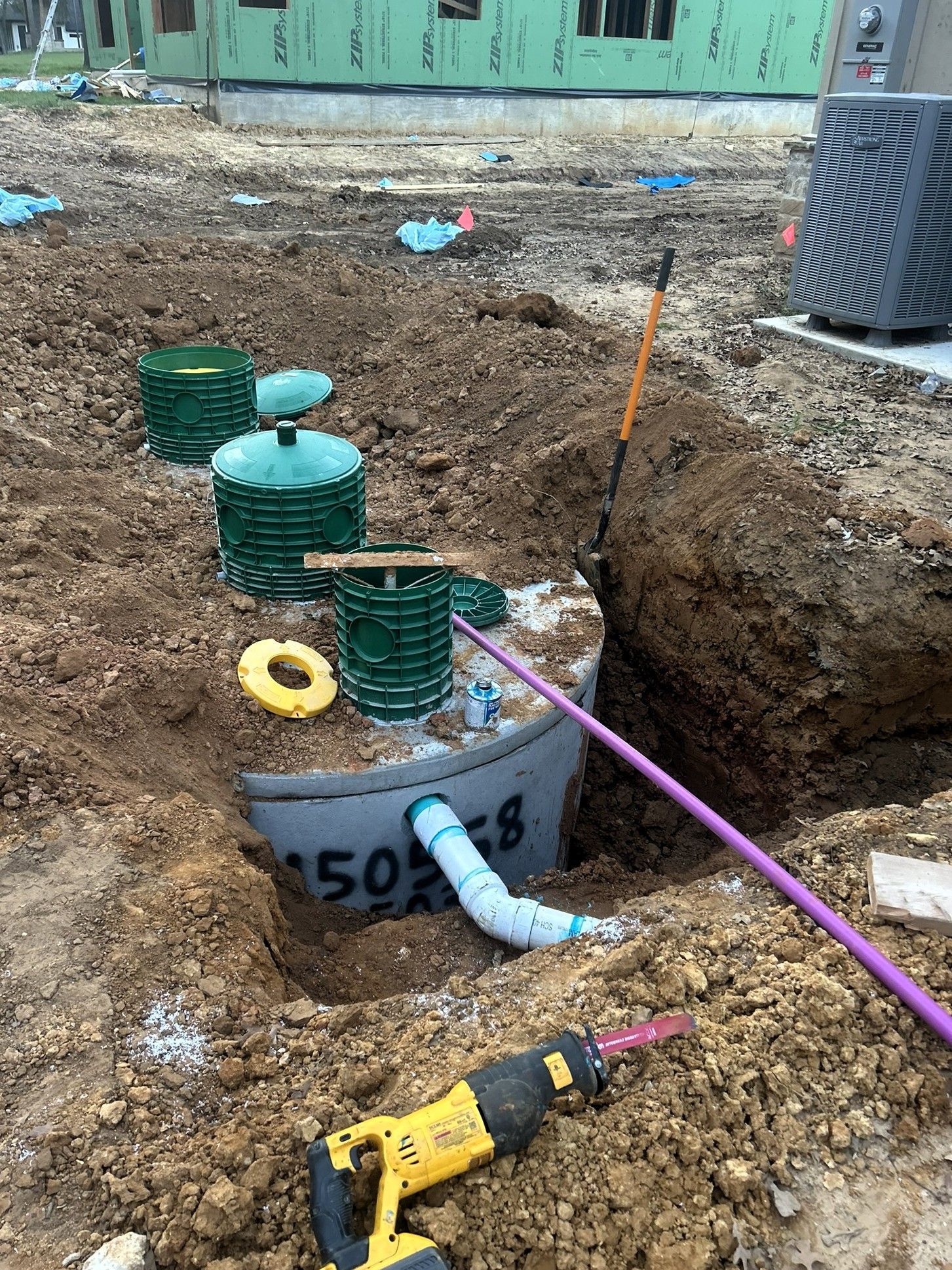 Construction trench with green utility caps, exposed white pipe, and tools beside a dirt excavation area.