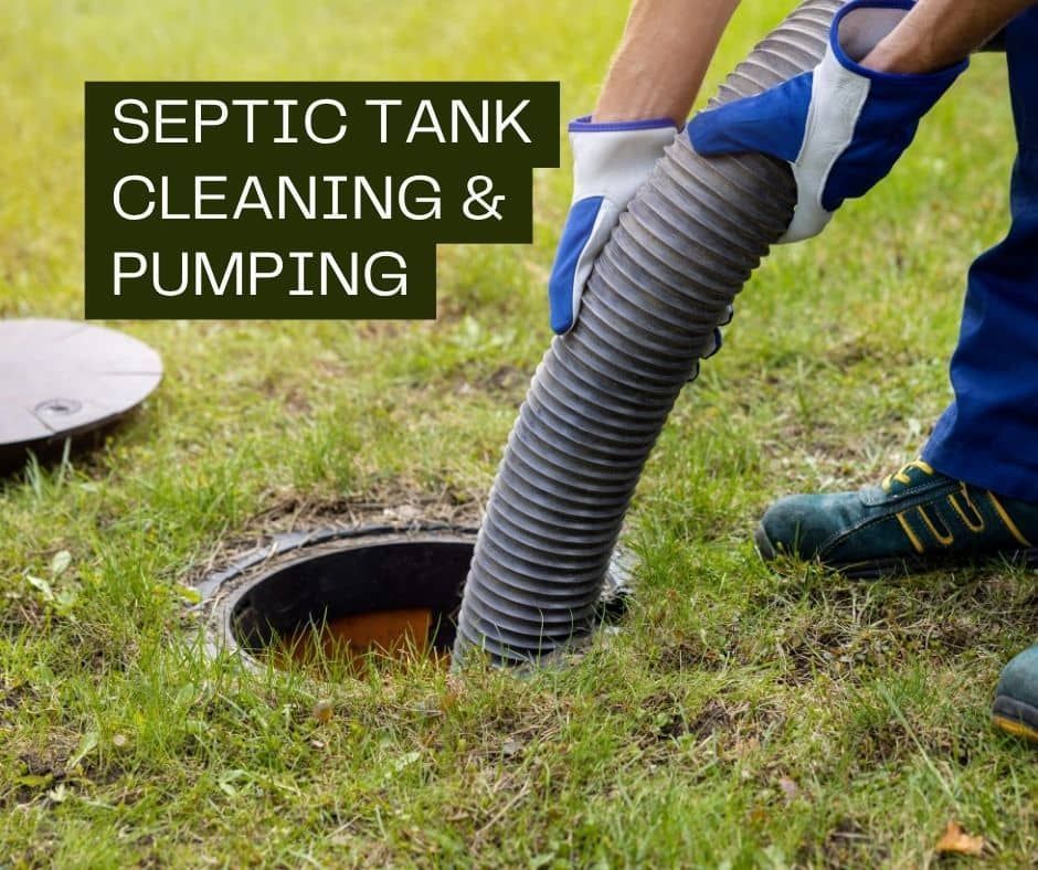 A worker in blue clothing uses a large vacuum hose to pump out an open residential septic tank in a grassy yard.