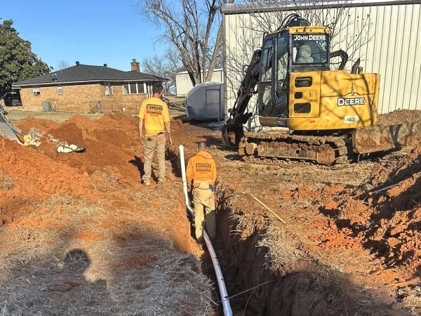 Workers and a yellow excavator digging a trench at a house construction site