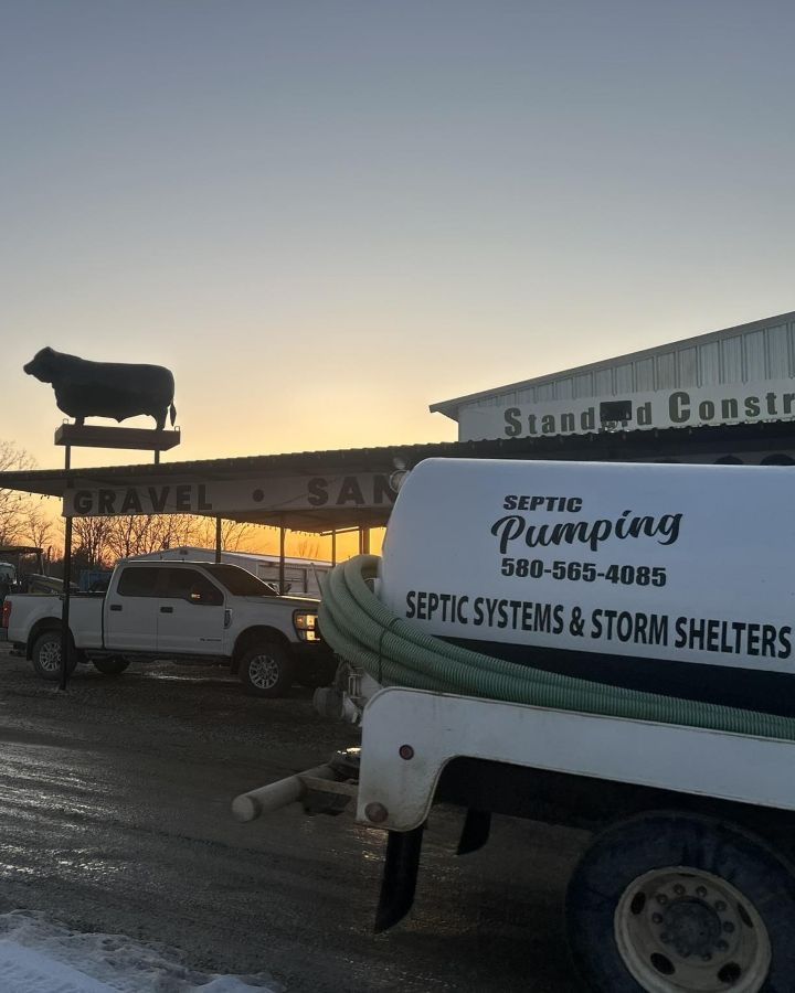 Standard Construction on Highway 70, Kingston, Oklahoma A septic pumping truck parked in front of a construction business with a metal cow silhouette on the roof at sunset.
