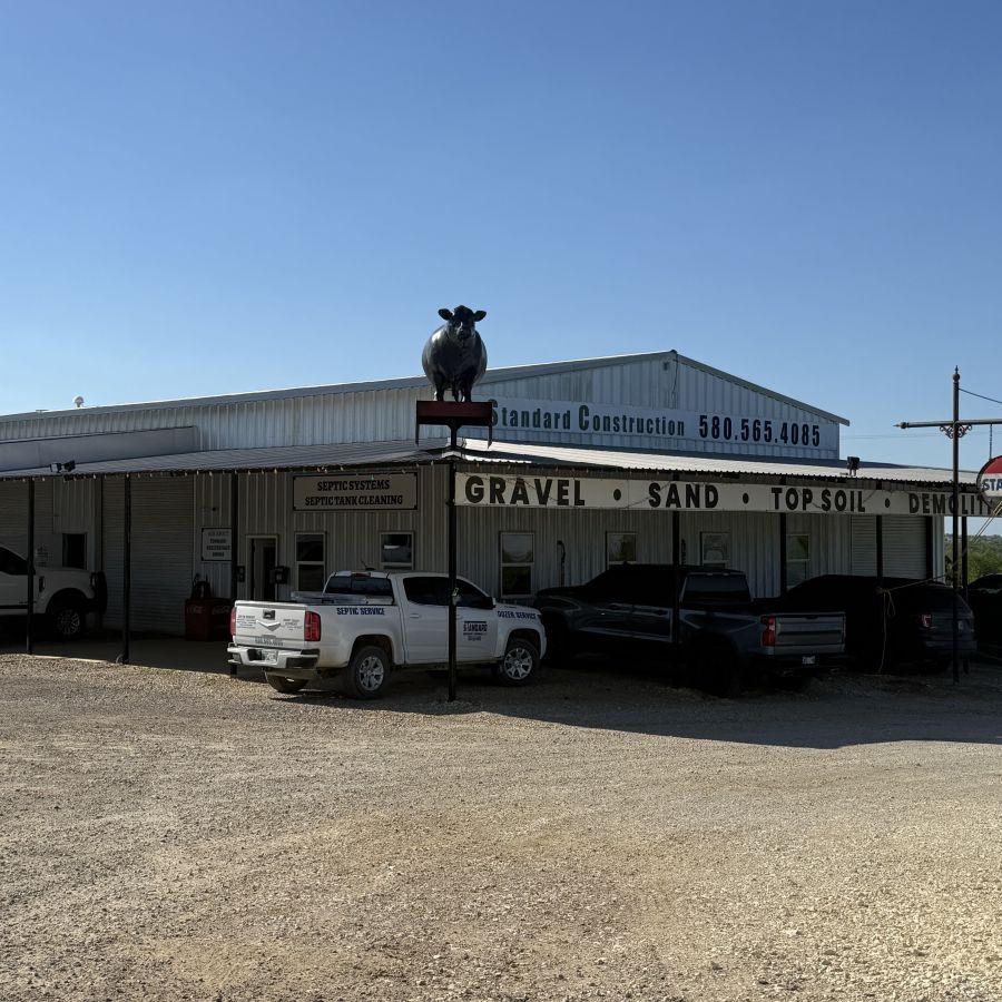 Gravel and sand store with a bull statue on the roof and parked trucks under a clear blue sky