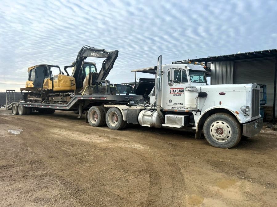 White semi-truck hauling a flatbed with two excavators at a dirt construction site