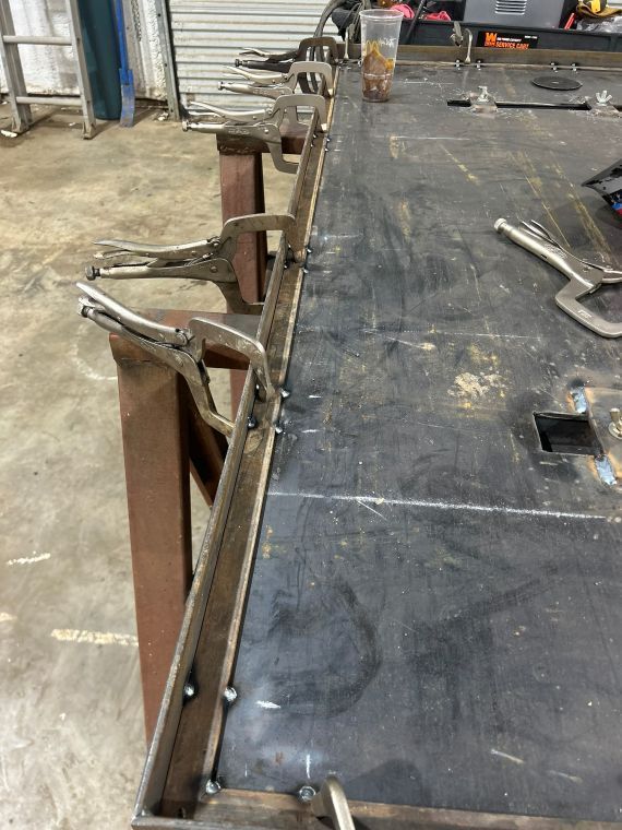 Workshop table with metal clamps holding a black work surface in place
