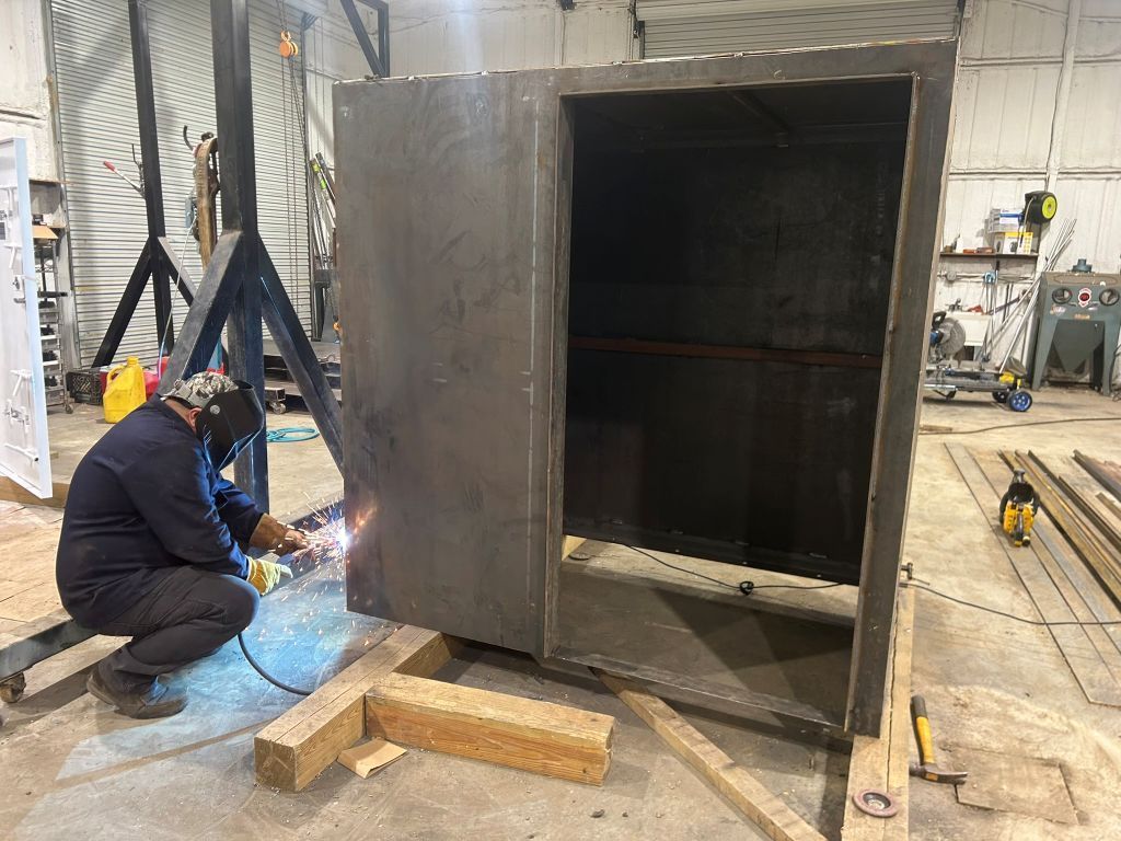 Worker welding a large metal cabinet in an industrial workshop, with sparks flying.