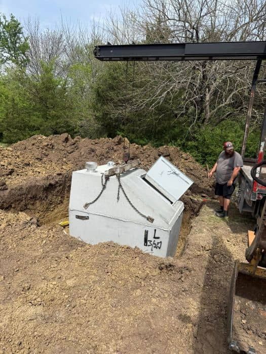 White concrete tornado shelter being installed into the ground in a hole.