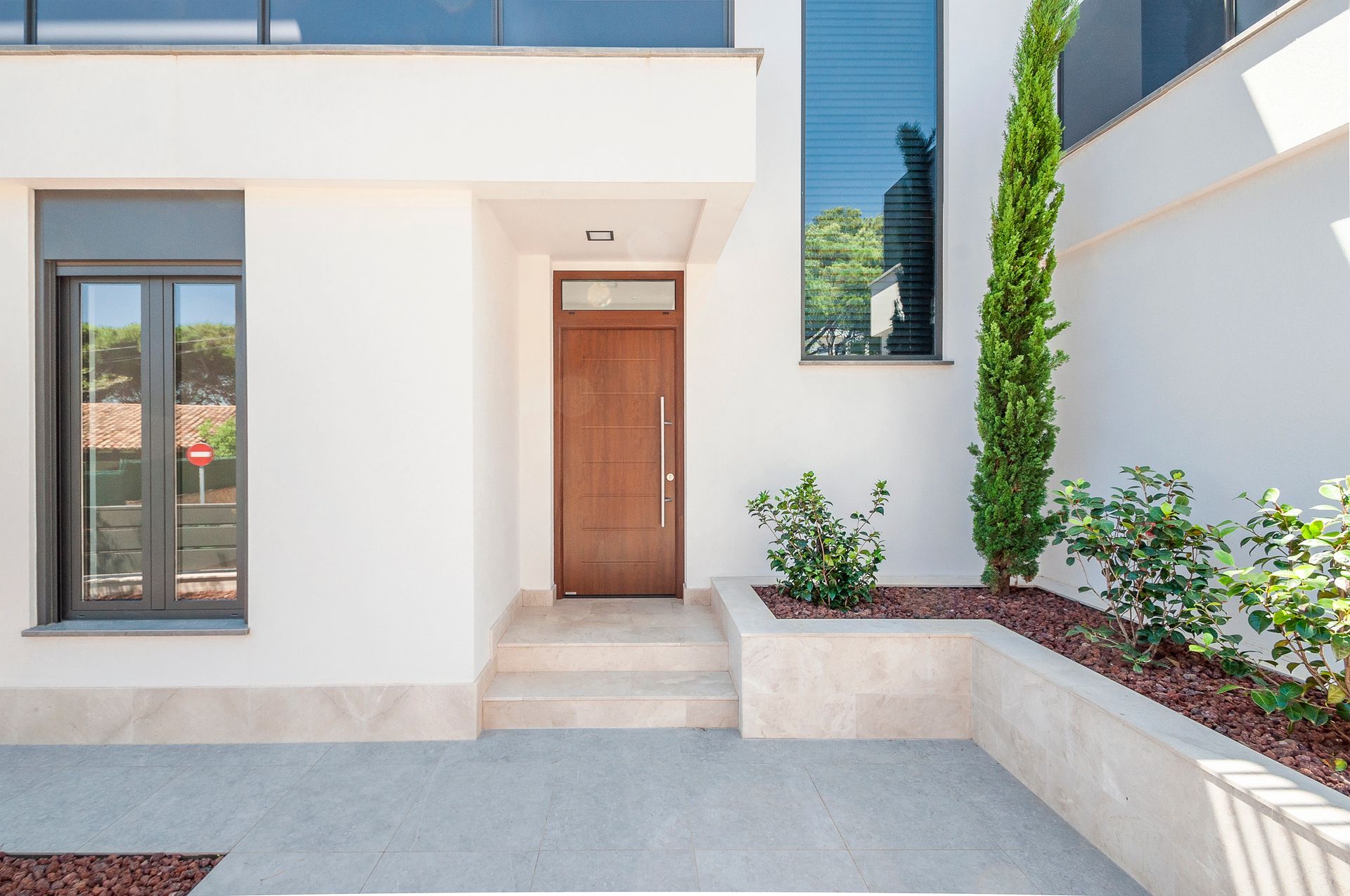 Ingresso moderno di una casa bianca con porta in legno, scalini e piccolo cortile paesaggistico.
