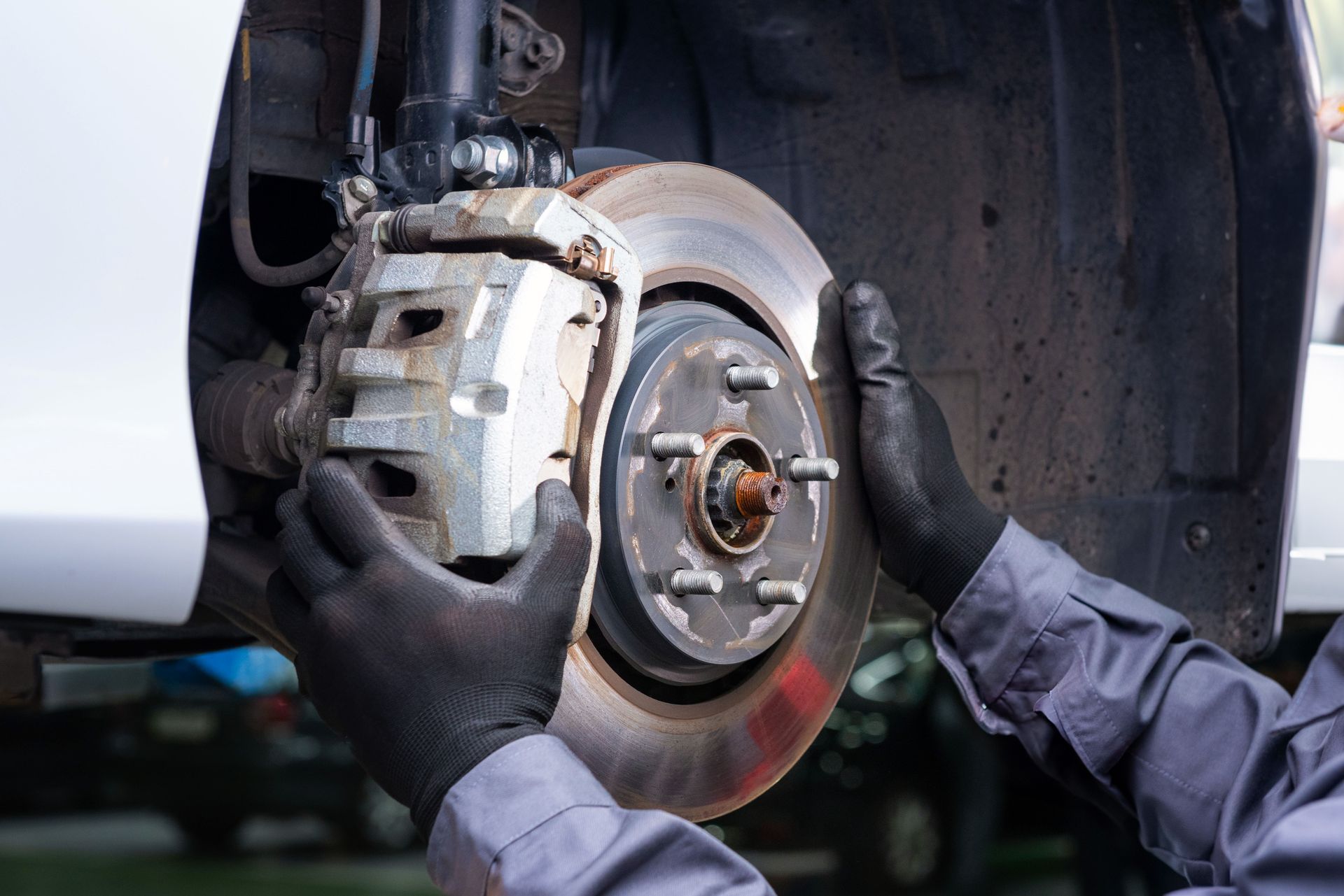 Mechanic in black gloves replacing a car brake rotor and caliper in a wheel well