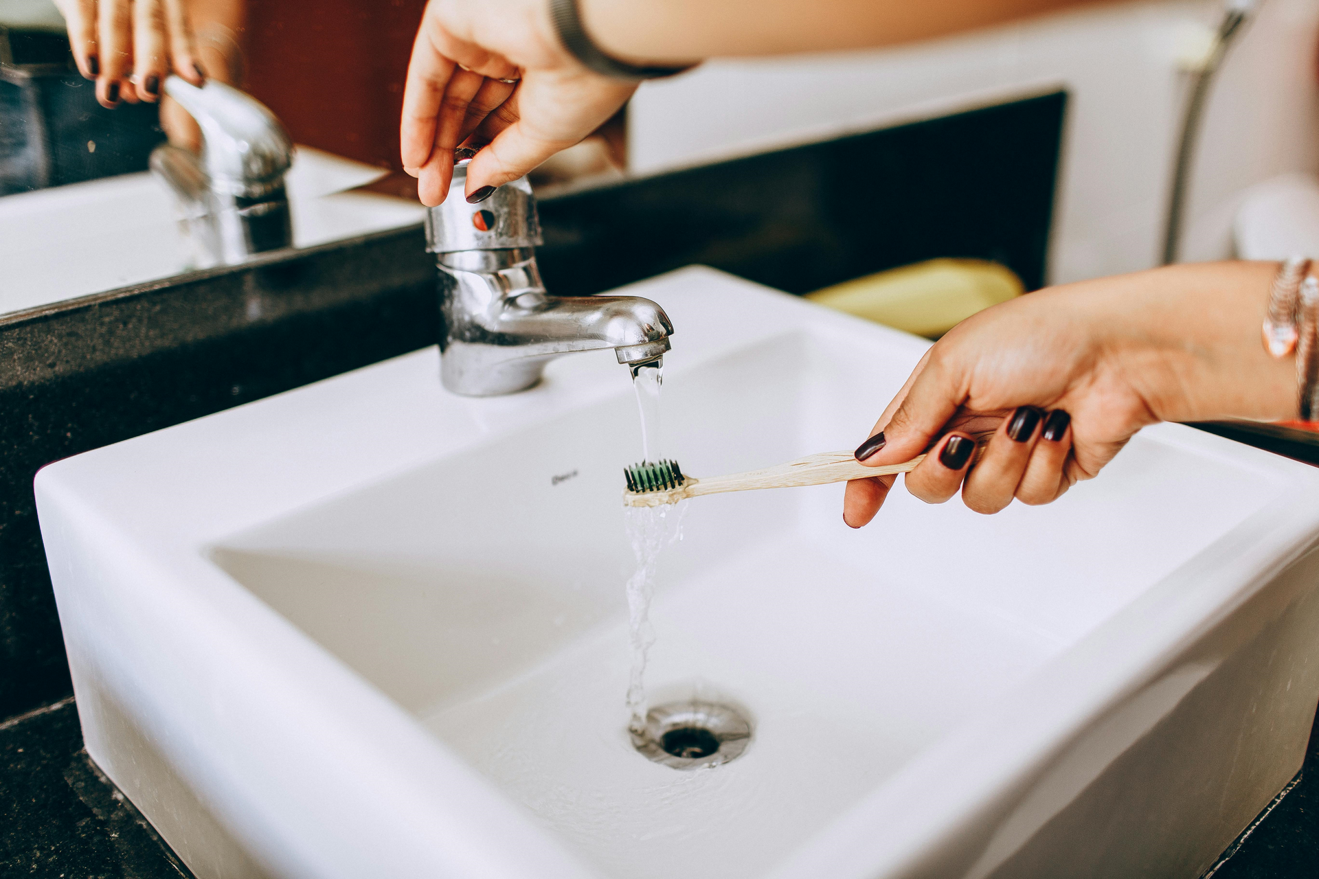 Hands brushing teeth at a white bathroom sink with running faucet