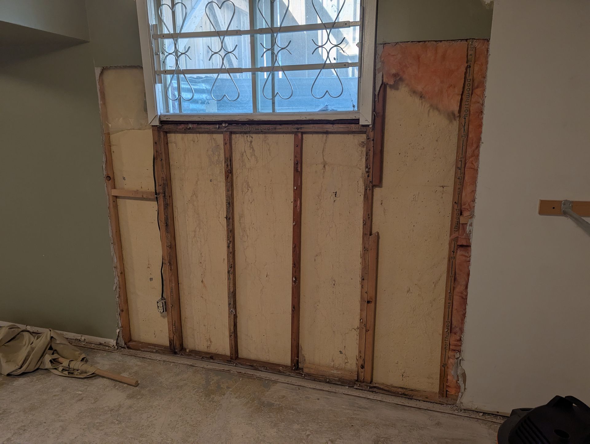 Partially renovated wall beneath a window, with exposed insulation and unfinished drywall