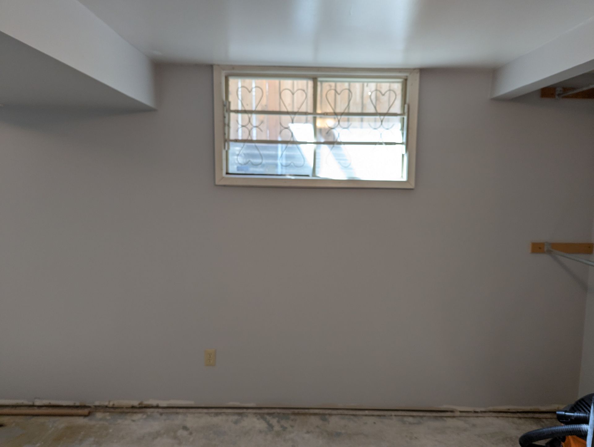 Bare basement room with gray walls, small window, and exposed floor trim.