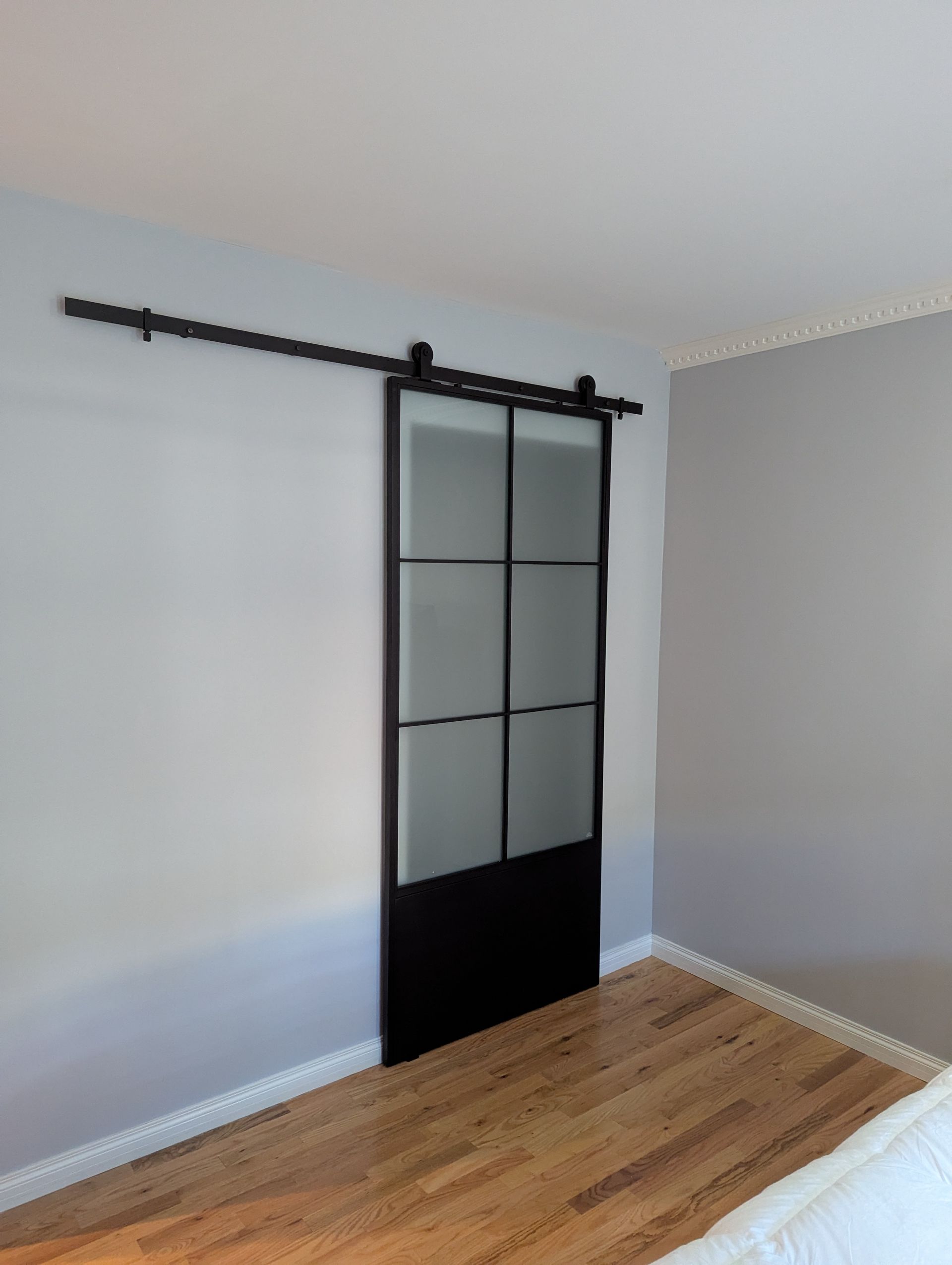 Empty room with white and gray walls, hardwood floor, and a black-framed sliding barn door.