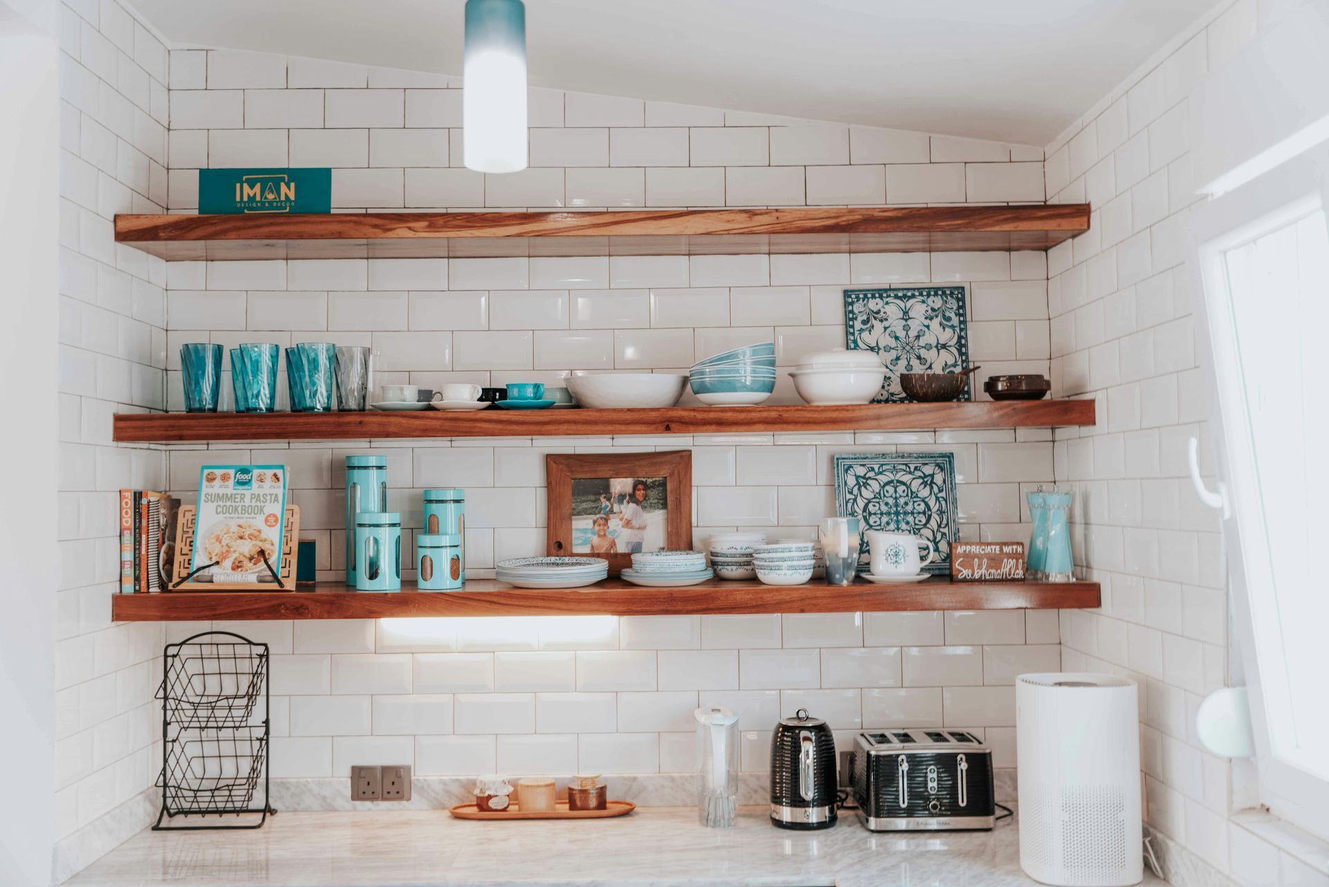White kitchen shelves with turquoise dishes, jars, decor, and coffee maker above a tiled counter