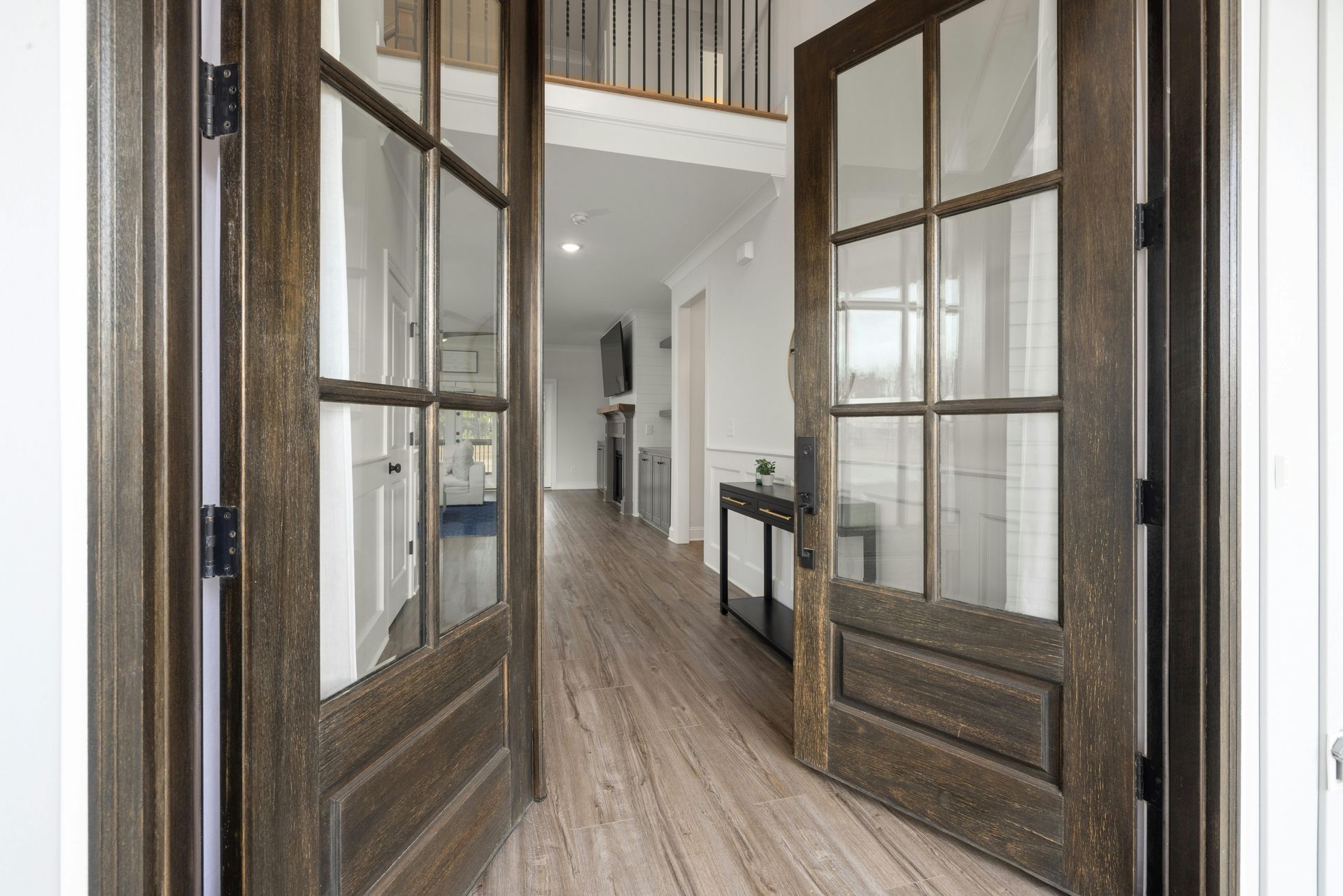 Open double wooden doors leading into a bright hallway with wood floors and glass panels