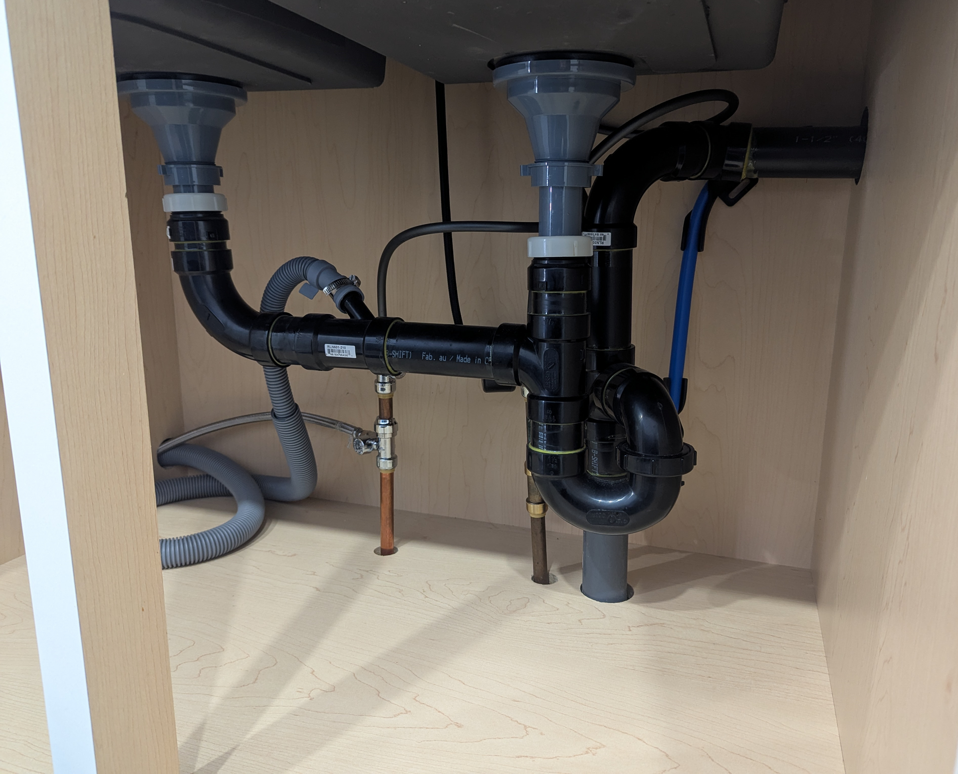 Under-sink plumbing with pipes, drain lines, and a black P-trap inside a cabinet