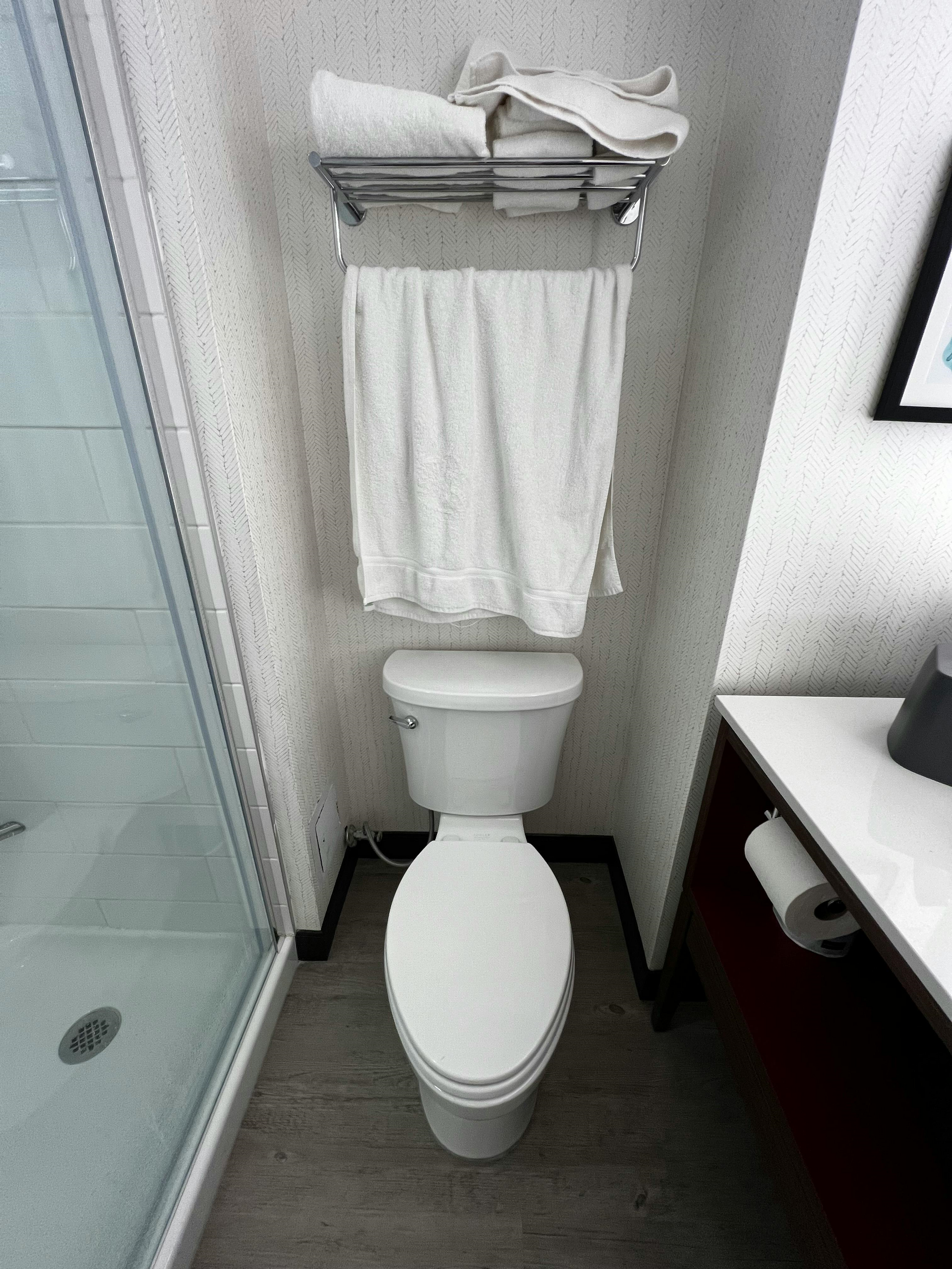 Small bathroom with toilet, towel rack, shower, and sink cabinet.