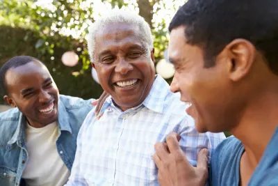 Three people smiling and laughing together outdoors in soft sunlight.