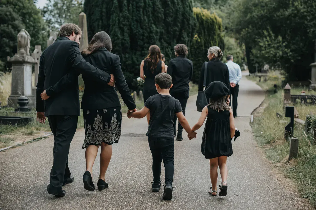 Mourning family walking hand in hand along a cemetery path