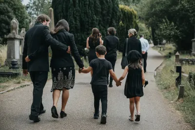 Mourning family walking hand in hand along a cemetery path