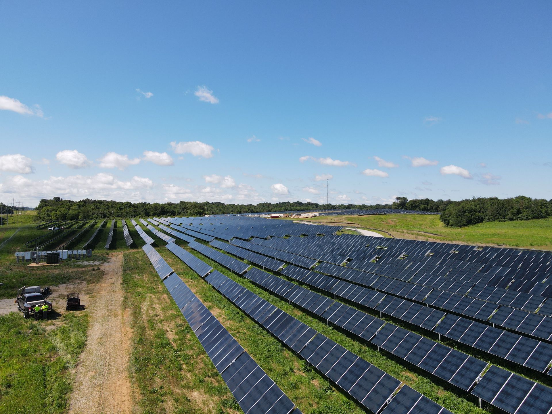 Rows of dark solar panels in a grassy field under a blue sky with scattered clouds