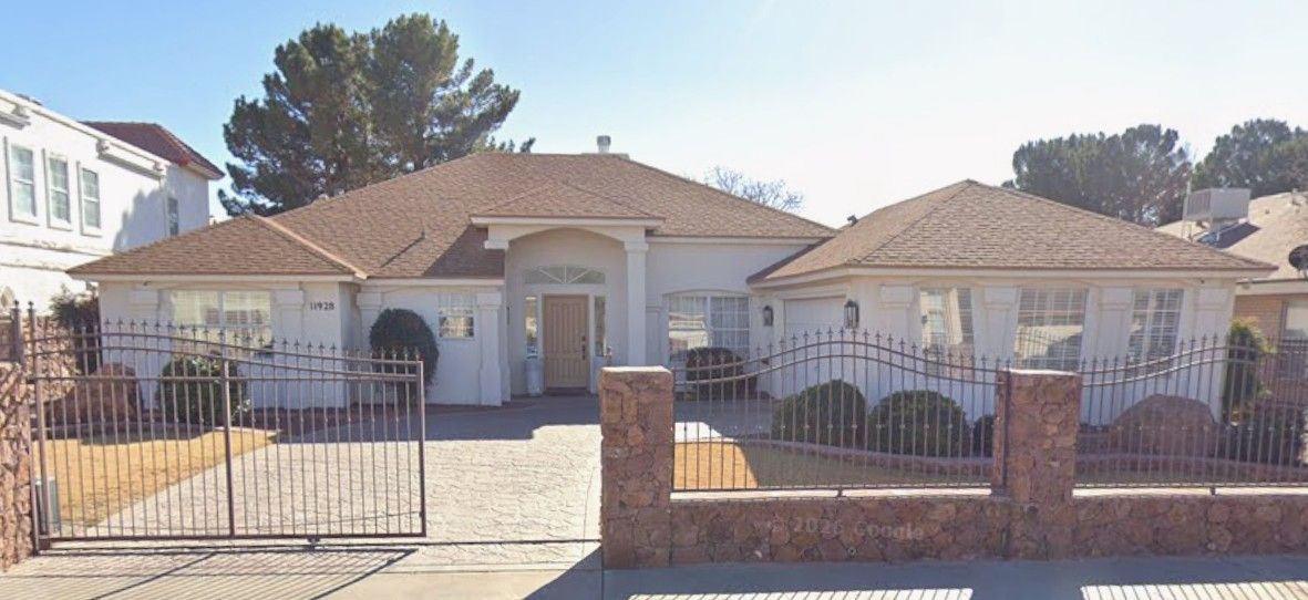 Single-story white house with a tiled roof, front gate, and brick fence in a sunny neighborhood