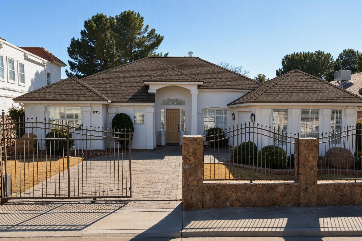 Single-story white house with a brown roof, gated front yard, and brick fence under a clear sky
