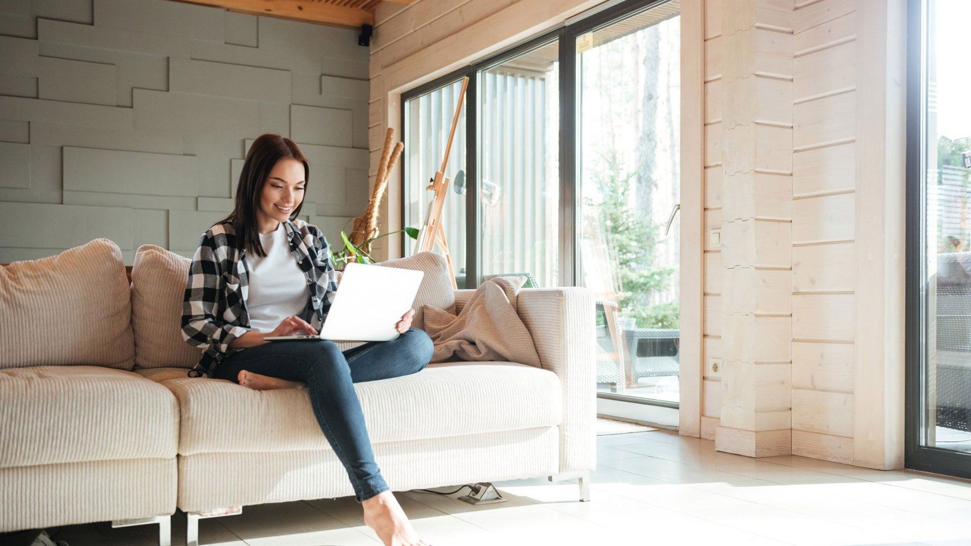 A woman sitting on a sofa looking at a laptop on her lap with on leg visible sitting on the other leg