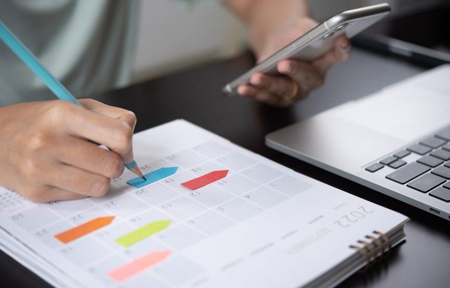 A person writing in a calendar while holding a cell phone 