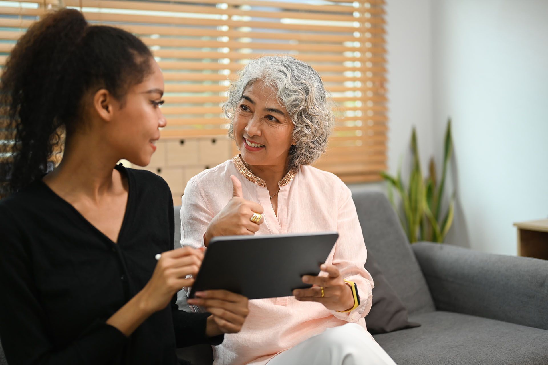 Two women are sitting on a couch looking at a tablet.