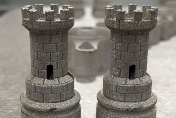 Two 3D-printed metal rook chess pieces, with a medieval tower design.