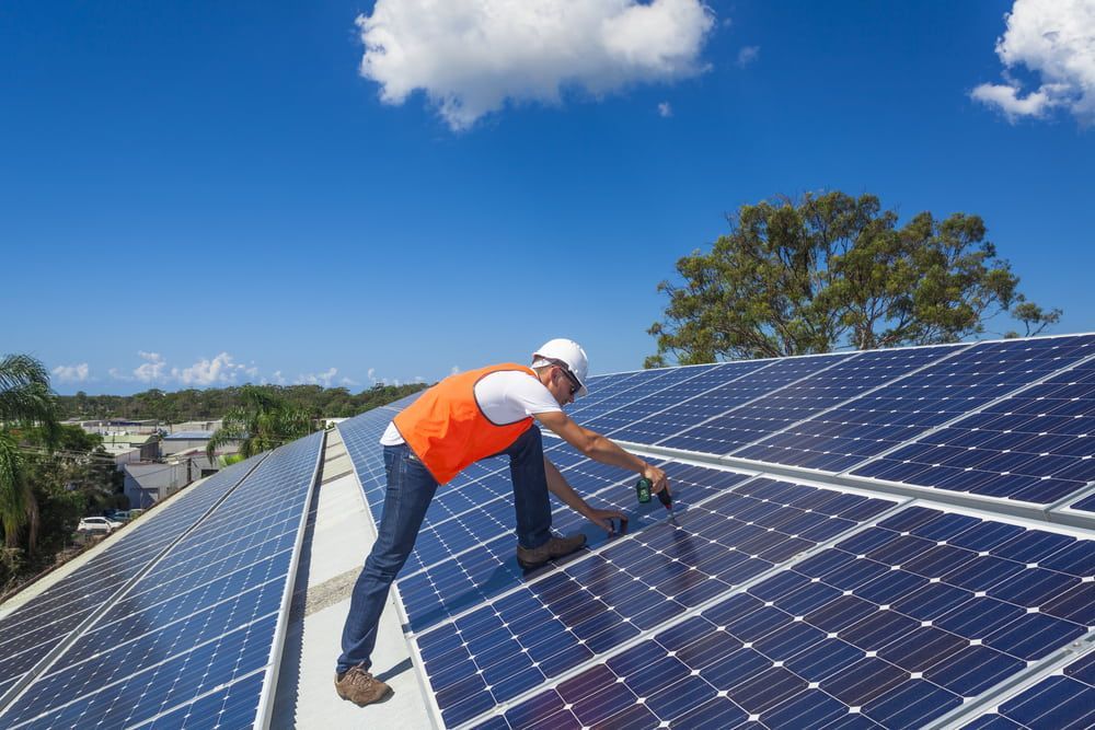A Man Is Installing Solar Panels On The Roof Of A Building — Evolution Solar Kingaroy in Kingaroy, QLD
