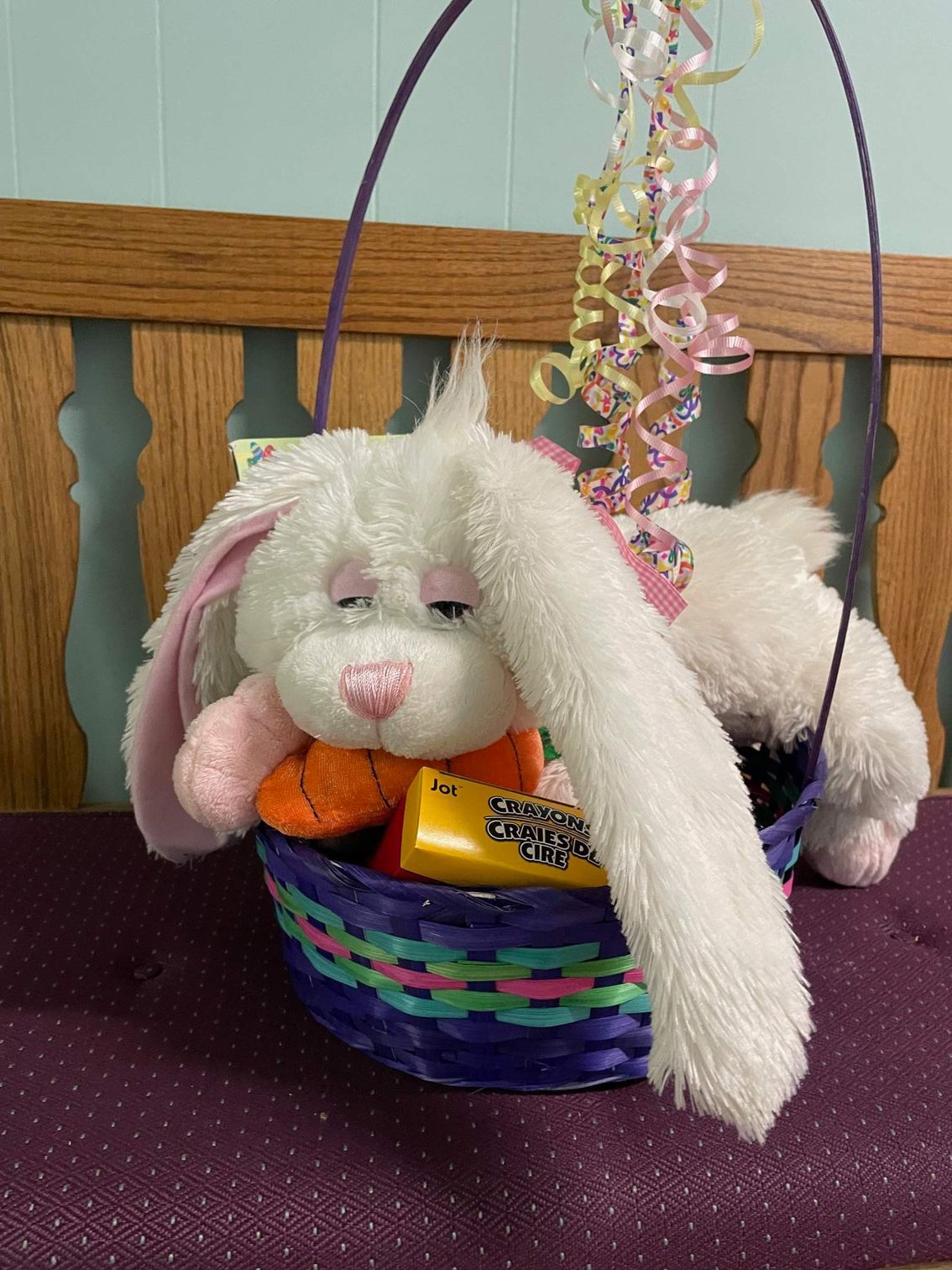 White stuffed bunny in purple Easter basket; carrots, crayons, and curly ribbon accents.