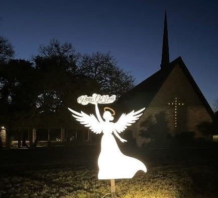 Silhouette of an angel statue holding a banner in front of a church at dusk.