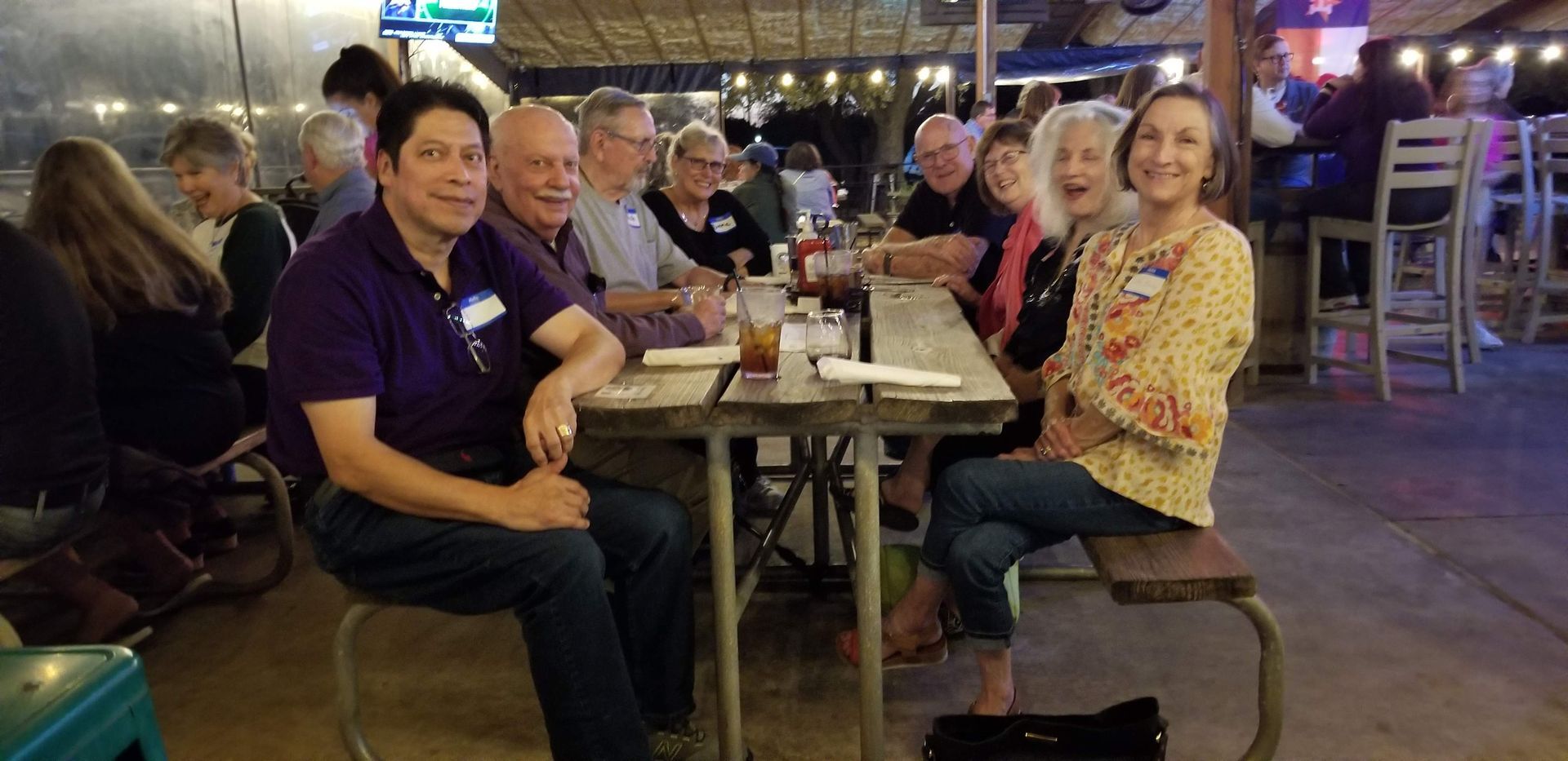 A group of people at a restaurant. They are sitting around a table, smiling, and looking at the camera.