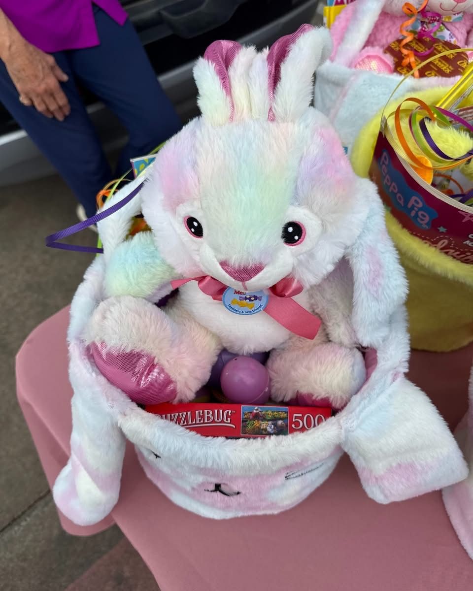 A plush pastel-colored bunny rabbit toy sits inside a matching bunny-themed Easter basket containing eggs and a puzzle.