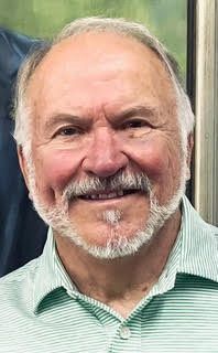 Man with graying hair and beard, wearing a light green collared shirt, smiling.
