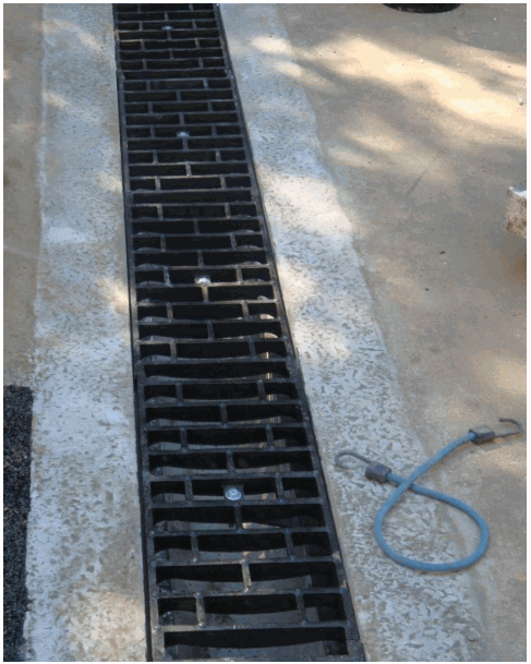 Black grate drain in concrete. Blue bungee cord nearby.