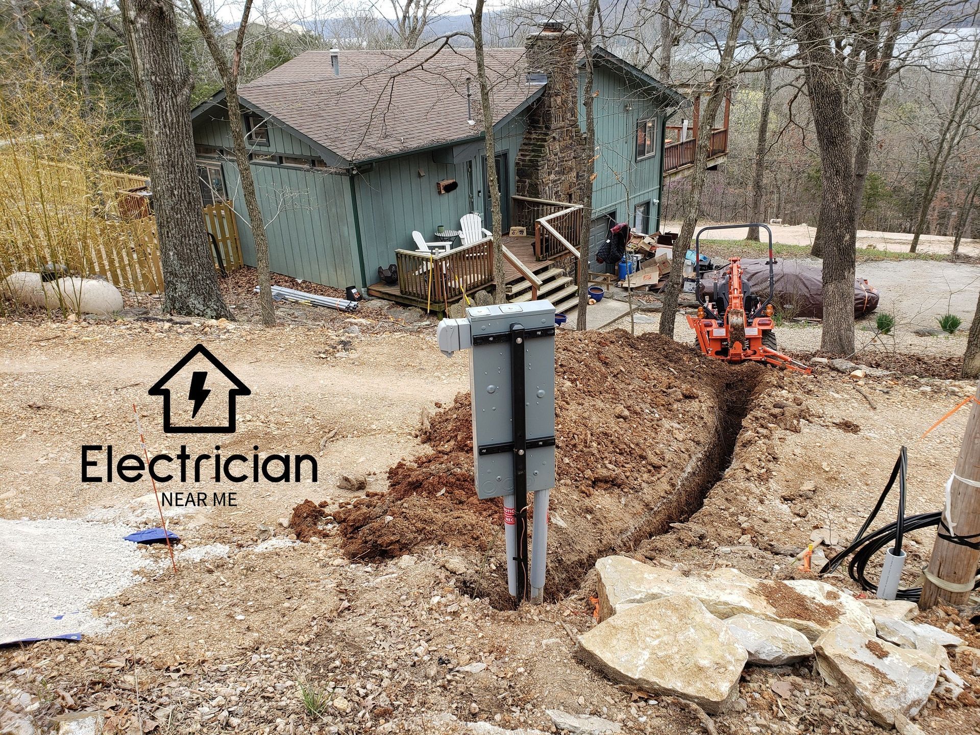 An electrician is digging a hole in the ground in front of a house.