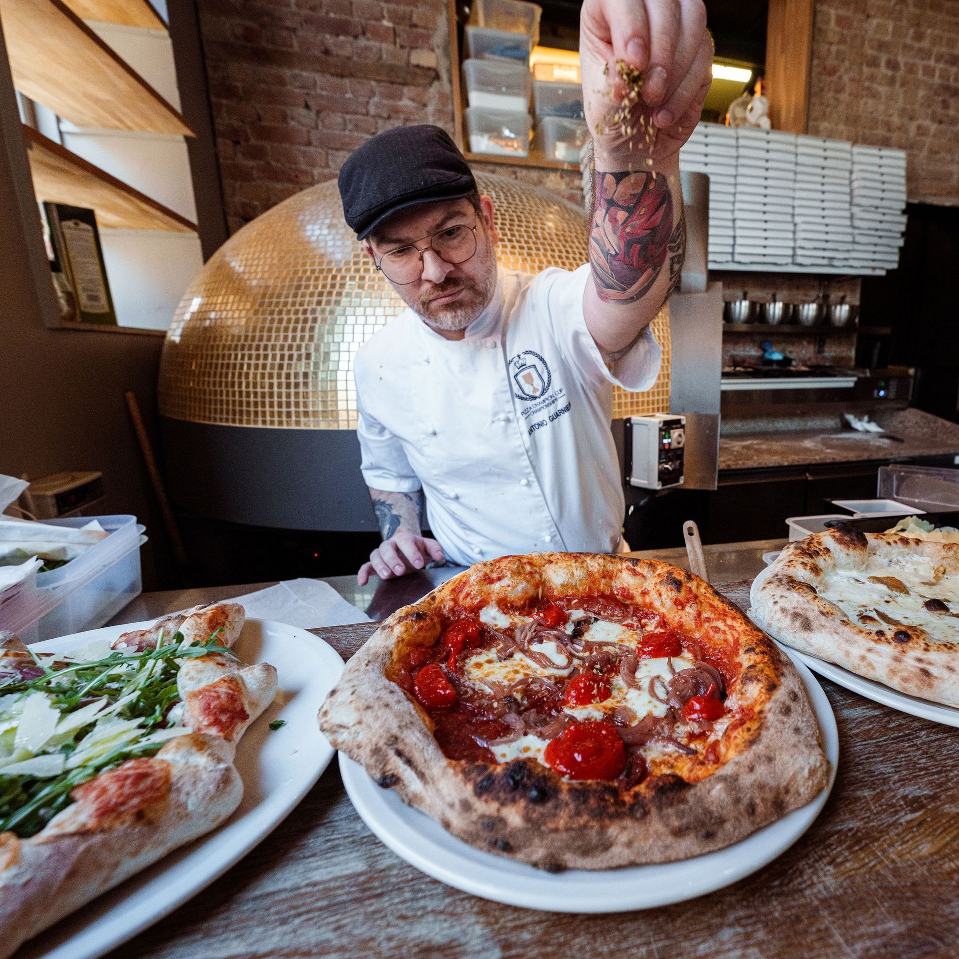 En mann i kokkeuniform legger pålegg på en pizza